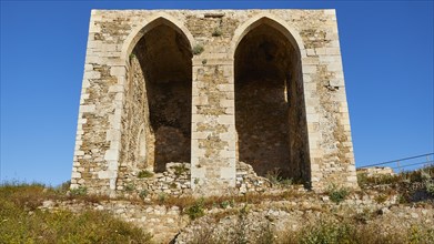 Two large arched windows in an old stone wall with a view of the blue sky, sea fortress of Methoni,