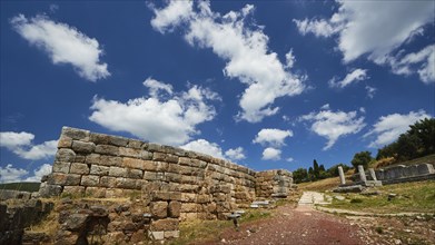 Path leads to ancient walled ruins under a cloudy blue sky, Ancient city wall, Archaeological site,
