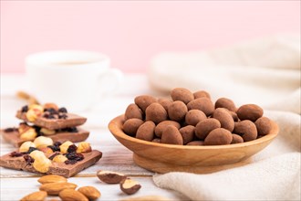 Almond in chocolate dragees in wooden plate and a cup of coffee on white and pink background and