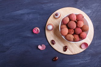 Lychee in a white plate on a black wooden background, top view, flat lay, copy space