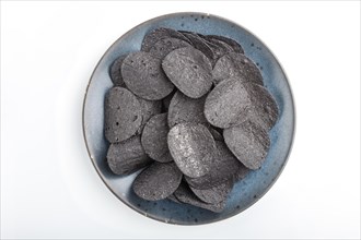 Black potato chips with charcoal on a blue ceramic plate isolated on white background. Top view,
