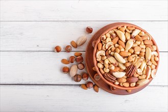 Mixed different kinds of nuts in ceramic bowl on white wooden background with copy space. hazelnut,