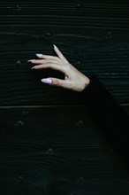 A hand with lavender nails against a dark wooden background evoking a mysterious elegance