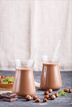 Organic non dairy hazelnut chocolate milk in glass and wooden plate with hazelnuts on a black