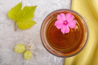 Glass of green grape juice with green textile and pink flower on a gray concrete background.