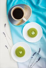 Green mousse cake with pistachio cream and a cup of coffee on a white wooden background and blue