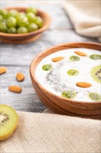 Yogurt with kiwi, gooseberry, chia and almonds in wooden bowl on gray wooden background and linen