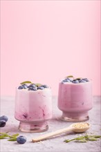 Yoghurt with blueberry and sesame in a glass and wooden spoon on gray and pink background. side