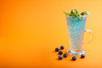 Glass of blueberry blue colored drink with basil seeds on orange background. Morninig, spring,