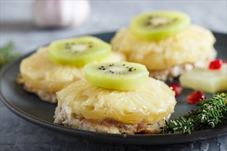 Pieces of baked pork with pineapple, cheese and kiwi on gray background, side view, close up,