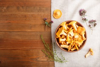 Chanterelle mushrooms in wooden bowl and spice herbs on wooden background with linen textile. top