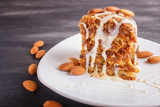 Pie with caramel, white milk sauce and almonds on a white plate on a black wooden background. close