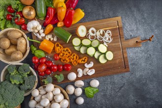 Various vegetables, peppers, tomatoes, onions, courgettes and broccoli arranged on a wooden board