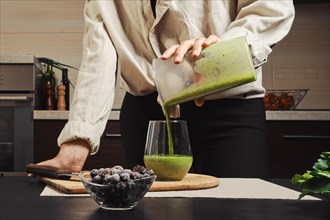 Unrecognizable woman pouring green smoothie in glass in the kitchen