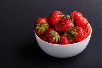 Fresh red strawberry in white bowl on black background. side view, close up