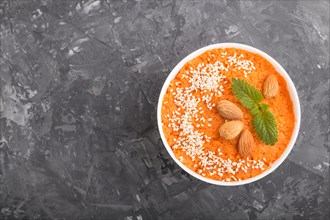 Carrot cream soup with sesame seeds and almonds in white bowl on a black concrete background. top