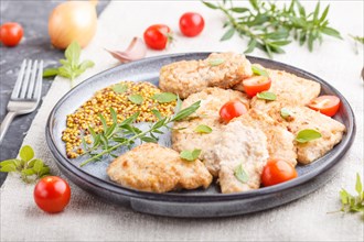 Fried pork chops with tomatoes and herbs on a gray ceramic plate on a black concrete background and