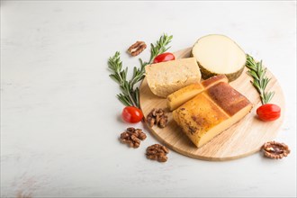 Smoked cheese and various types of cheese with rosemary and tomatoes on wooden board on a white