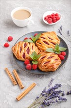 Puff pastry buns with strawberry jam on blue ceramic plate on gray concrete background, cup of