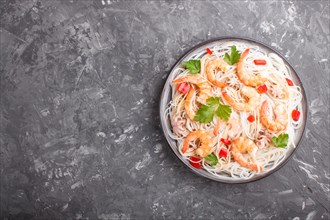 Rice noodles with shrimps or prawns and small octopuses on gray ceramic plate on a black concrete