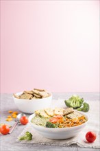 Green broccoli cream soup with crackers and cheese in white bowl on a gray and pink background and