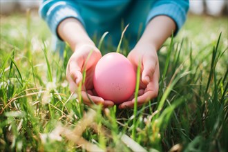 Child's hands holding large pink Easter egg in grass. KI generiert, generiert AI generated
