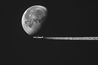 Aeroplane with contrails in front of a waning moon in the early morning sky, Bavaria, Germany, no