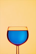 A clear wine glass with a calm blue liquid paired with a yellow background