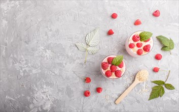 Yoghurt with raspberry and sesame in a glass and wooden spoon on gray concrete background. top