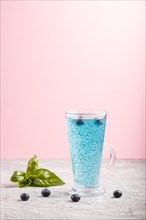 Glass of blueberry blue colored drink with basil seeds on a gray and pink background. Morninig,