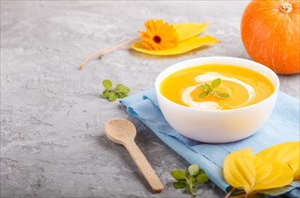 Traditional pumpkin cream soup with in white bowl on a gray concrete background with blue napkin.