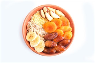 A plate with muesli, banana, dried apricots, dates, Brazil nuts isolated on a white background. top