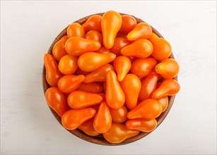 Fresh orange grape tomatoes in wooden bowl on white wooden background. top view, flat lay, close up