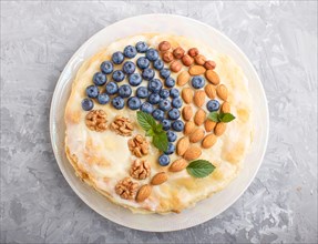 Homemade layered Napoleon cake with milk cream. Decorated with blueberry, almonds, walnuts,