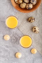 Sweet egg liqueur in glass with quail eggs and meringues on a gray concrete background. Top view,