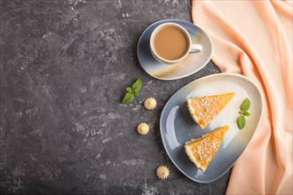Two pieces of traditional american pumpkin pie with cup of coffee on a black concrete background