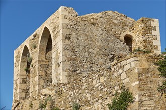 Part of an old stone fortress ruin with two arched windows in front of a blue sky, sea fortress