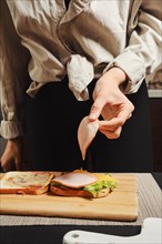 Unrecognizable woman puts slice of ham on sandwich