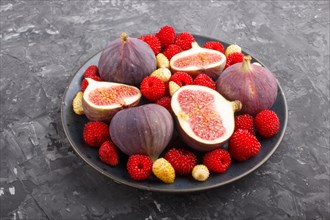 Fresh figs, strawberries and raspberries on blue ceramic plate on black concrete background. side