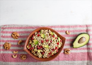 Salad of germinated buckwheat, avocado, walnut and pomegranate seeds in clay plate on white wooden