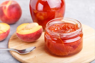 Peach jam in a glass jar with fresh fruits on gray concrete background. side view, close up