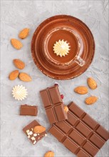 Cup of hot chocolate and pieces of milk chocolate with almonds on a gray concrete background. Flat