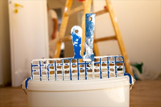 Symbolic image of painting work: Close-up of a paint bucket with scraper grid, in the background a