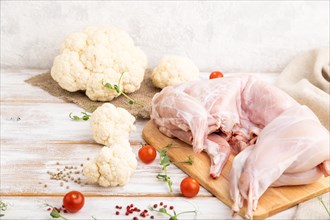 Whole raw rabbit with cauliflower, tomatoes and spices on a white wooden background and linen