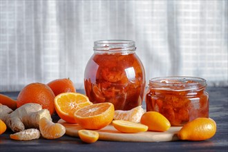 Tangerine and kumquat jam in a glass jar with fresh fruits on a black wooden table and white linen