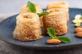 Kunafa, traditional arabic sweets in blue ceramic plate on a gray concrete background. side view,