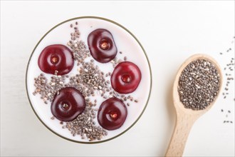 Yoghurt with cherries, chia seeds and granola in glass with wooden spoon on white wooden background