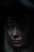 A dark, intimate portrait of a woman partially obscured by her hat