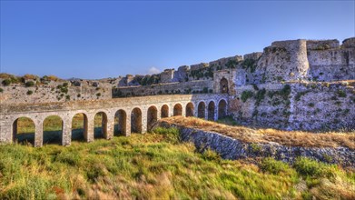 Sunlit view of an old fortress with an aqueduct over green hills, sea fortress Methoni,