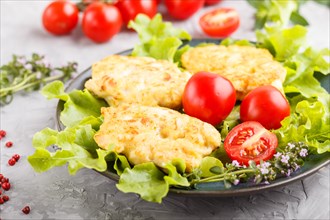 Minced chicken cutlets with lettuce, tomatoes and herbs on a gray concrete background. side view,
